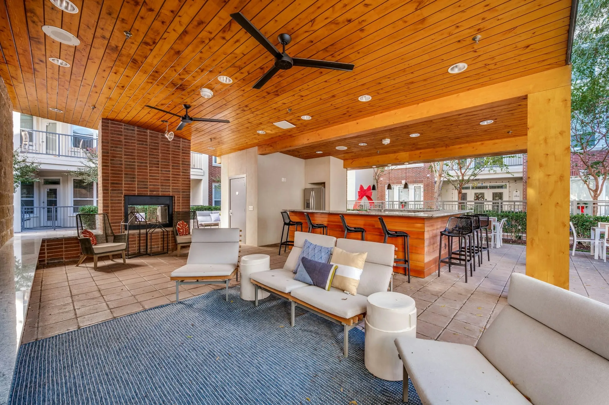 AMLI Frisco Crossing - Shaded outdoor lounge area with ceiling fans, cushioned seating, brick fireplace, and bar at AMLI Frisco Crossing apartments