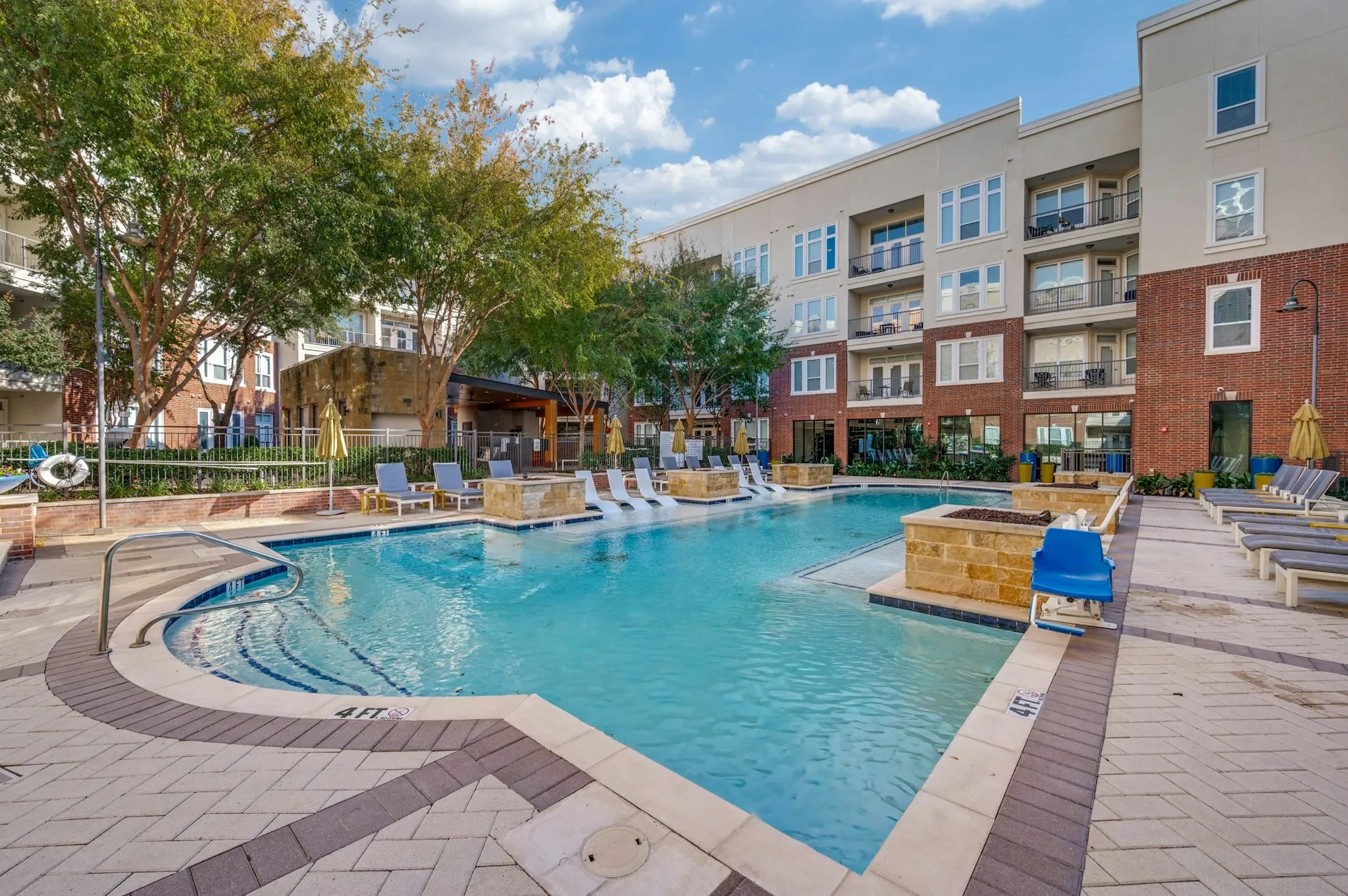 AMLI Frisco Crossing - Resort-style swimming pool with white in-water loungers, umbrellas, cushioned seating and brick buildings at AMLI Frisco Crossing apartments