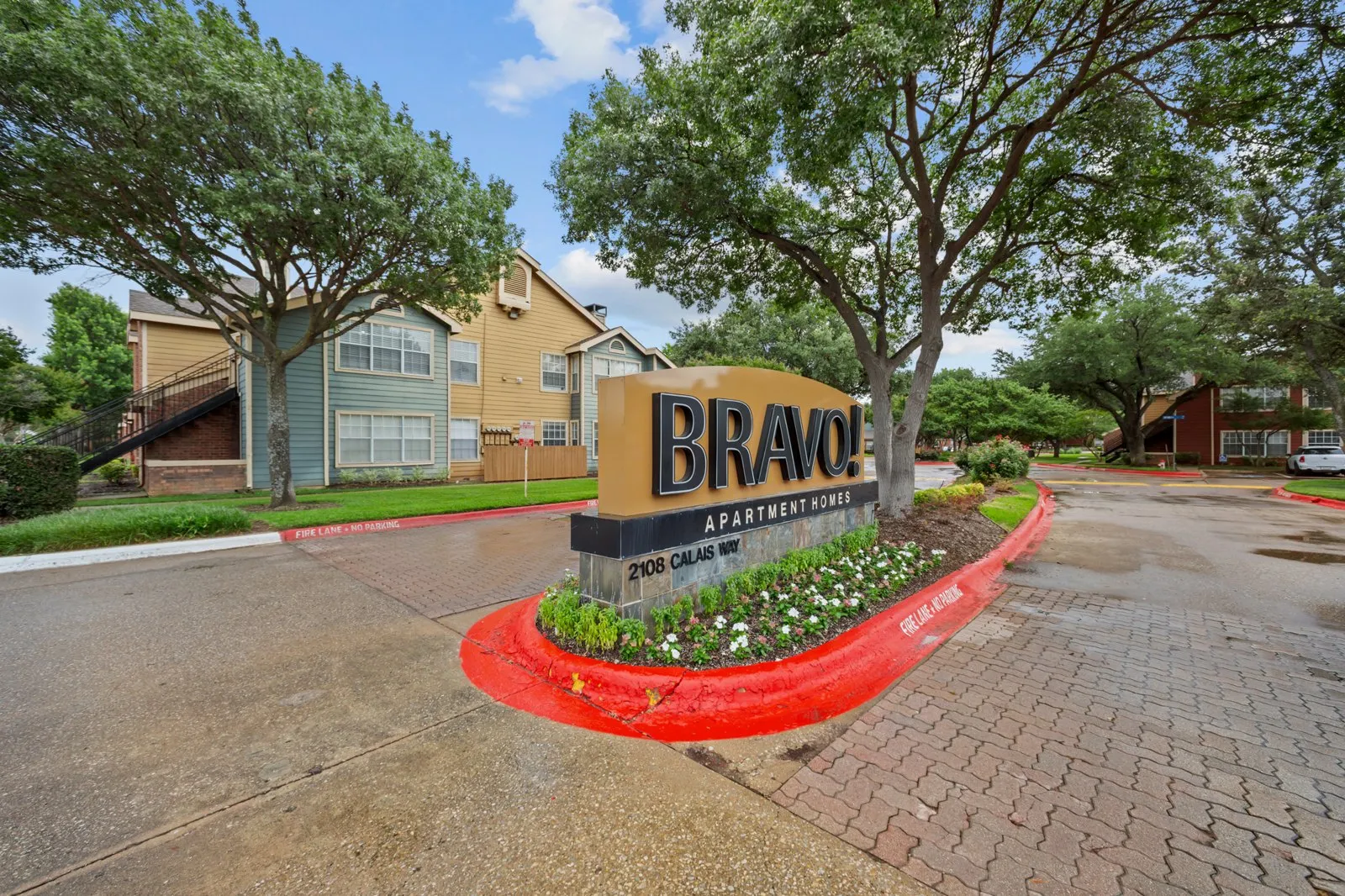 A sign for Bravo Apartments is in front of some trees and buildings. at Bravo Apartment Living