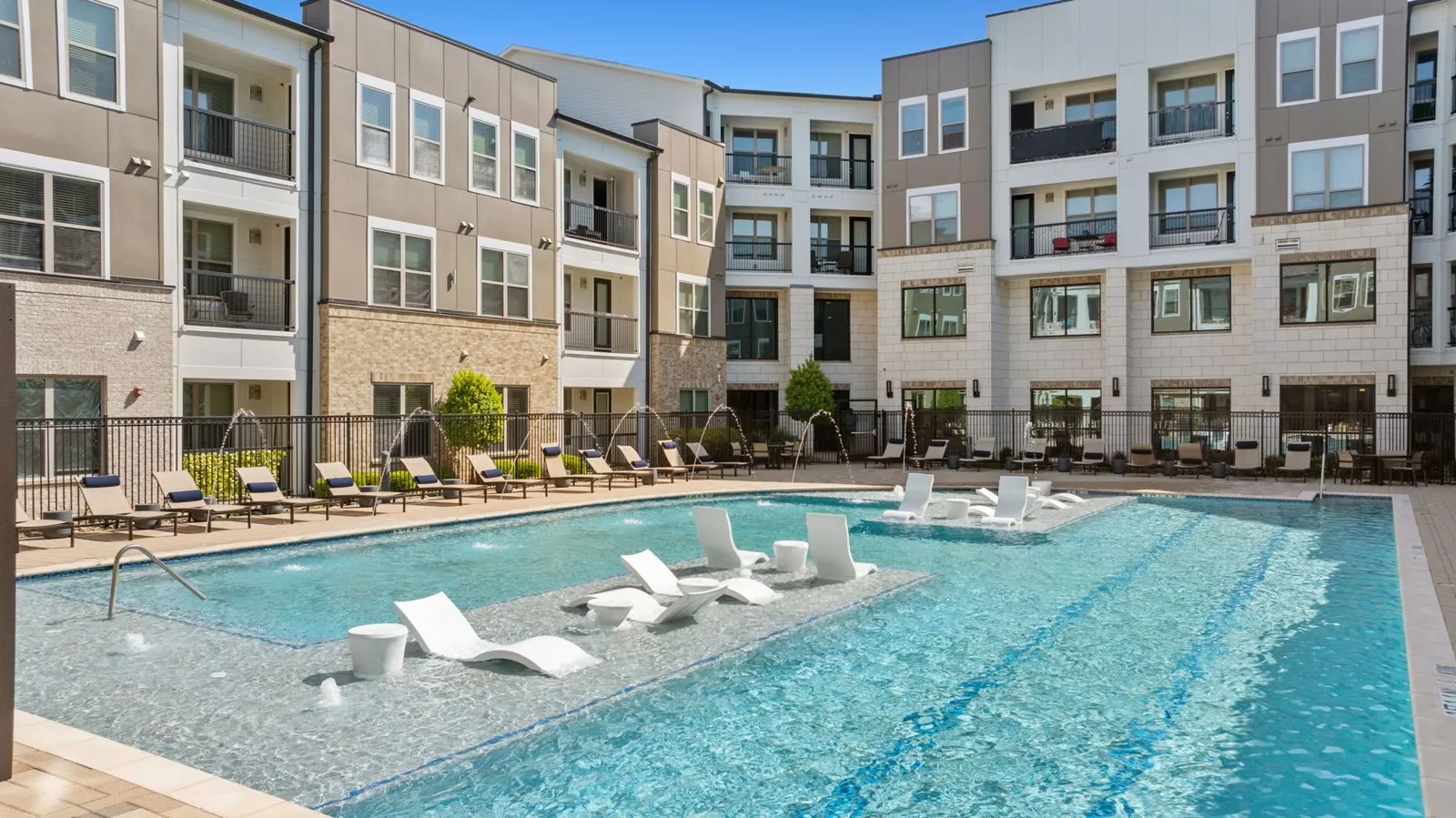 A large swimming pool with lounge chairs in front of apartment buildings. at Axis at Watters Creek