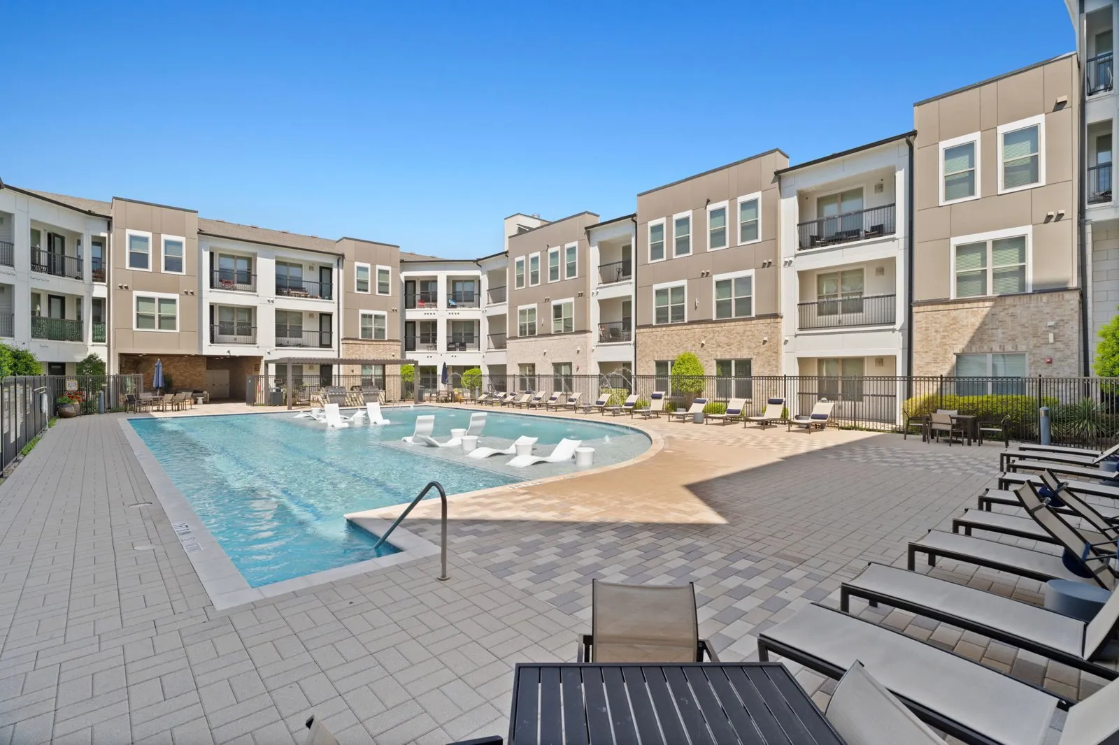 A swimming pool surrounded by apartment buildings and lounge chairs. at Axis at Watters Creek