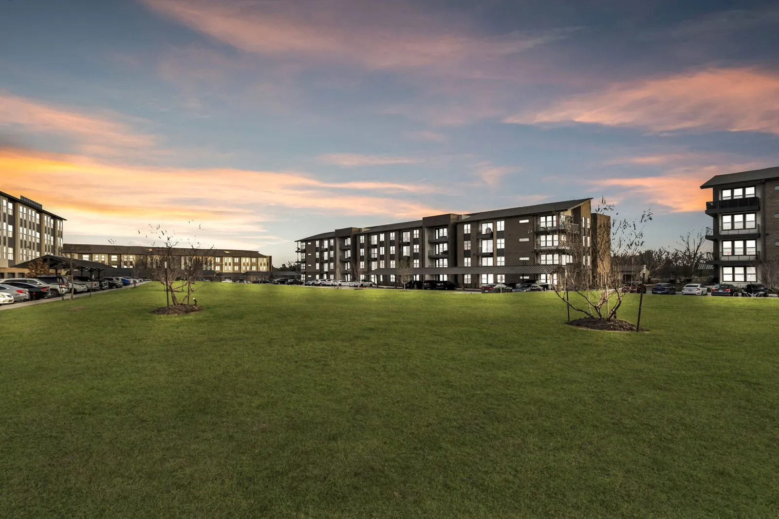A large grassy field in front of a building with a sunset in the background. at Axis Grand Crossing